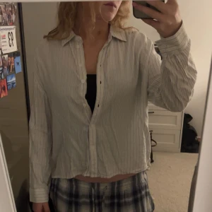 Ljusrandig skjorta med knappar fran Lee - Säljer en ljus, randig skjorta med klassisk krage och långa ärmar. Skjortan har knappar framtill och är lite loose i passformen, perfekt att slänga över ett linne. Materialet känns lätt och skönt mot huden, troligen bomull. Enkel och chill stil.