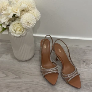  klackar - Snygga pumps från Zara i brun ton med transparenta detaljer och glittriga remmar. Skorna har spetsig tå, öppen häl och hög klack. Perfekta för dig som gillar att sticka ut med stilrena och trendiga skor. Storlek 36.