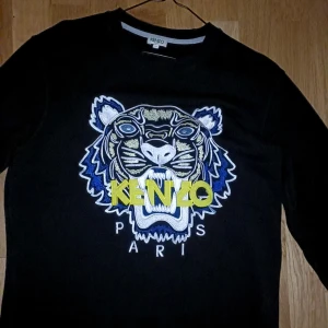 Svart Kenzo riktigt fin tröja st S  - Svart sweatshirt från Kenzo med ikonisk broderad tiger på bröstet i blått, vitt och gult. Tröjan har rund hals, långärmad passform och ribbade muddar. Perfekt statement-plagg med cool Paris-vibe och snygga färgdetaljer. Tagit väl hand om den så den är i mycket bra skick som ny ,inga skador osv ..äkta tröja ! Köptes för 3999 säljes för 700