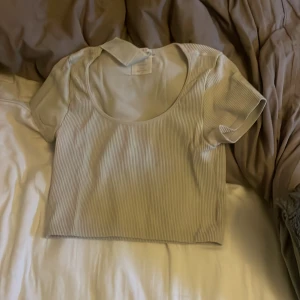 Ljusbeige ribbad croppad topp - Säljer en ljusbeige croppad topp med ribbad struktur och rundad halsringning. Toppen har korta ärmar och är tillverkad i ett mjukt, stretchigt material som sitter snyggt på kroppen. Perfekt för dig som gillar minimalistisk och clean stil.