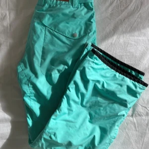 Turkosa täckbyxor från Warp - Turkosa täckbyxor från Warp med svarta detaljer vid benslut, dragkedjor vid fickor och justerbar midja. Perfekta för vinterns aktiviteter. Byxorna har flera praktiska fickor och är fodrade för extra värme. Jag har använt dem som skidbyxor tills de inte passade längre och har nu bara legat i garderoben efter jag köpte nya för några år sedan. Har varit super bra och fungerade perfekt senast jag använde dem förutom storleken för mig. 