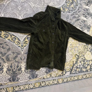 Grön manchester overshirt från Uniqlo. På etiketten står de xs fast det passar bäst S eller M - Säljer en mörkgrön overshirt från Uniqlo i mjuk manchester. Jackan har klassisk krage, två bröstfickor med knappar och långa ärmar. Perfekt att slänga på över en hoodie eller t-shirt för en chill look. Passar dig som gillar stilren och enkel design. Produkten är samt gjord av 100% japansk tyg där man kan känna både kvalitet och värmen som den bär.