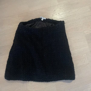 Svart kortkjol i bouclé från Other Stories - Säljer en svart kortkjol från Gina Tricot i bouclé-liknande material. Kjolen har en rak passform och är helfodrad för extra komfort. Perfekt att styla med boots eller en stickad tröja för en trendig look.