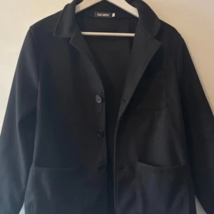 Svart overshirt  - Säljer en svart overshirt från Flex Supply i storlek S. Den har något kortare armar men är i väldigt fint skick! Nypris 500kr. Klassisk design med krage, tre knappar framtill och stora fickor på sidorna. Jackan har lång ärm och är tillverkad i ett mjukt material som ger en clean och stilren look.