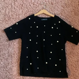 Svart stickad tröja med pärlor från Zara - Svart stickad tröja från Zara med kort ärm och coola pärldetaljer över hela tröjan. Perfekt för dig som vill ha något extra i din outfit. Rund halsringning och rak passform.