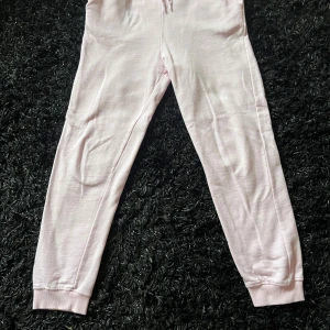 Ljusrosa mjukisbyxor med snörning - Säljer ett par ljusrosa mjukisbyxor från 157 i storlek 160. Byxorna har ribbad midja med snörning, sidofickor och muddar vid bensluten. Mjukt och skönt material, perfekt för chill dagar. Fleece på insidan för extra komfort.är små i storlek 