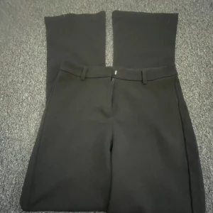 Svarta kostymbyxor från Vero Moda - Stilrena svarta kostymbyxor från Vero Moda i storlek S/32. Byxorna har utsvängda ben, bälteshällor och stängs med dragkedja och knapp framtill. Perfekta för en clean och klassisk look, passar till både sneakers och boots.