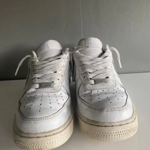 Nike Air Force 1 vita sneakers - Klassiska vita Nike Air Force 1 sneakers i skinn med perforerad tå, snörning och låg profil. Snygg och tidlös modell med Nike-logga bak och på plösen. Perfekta för dig som gillar streetstyle och vill ha en ikonisk sneaker i garderoben. Är ett litet hål i sulan, se bild 5. Går att prata pris jag bara la ett förslag.