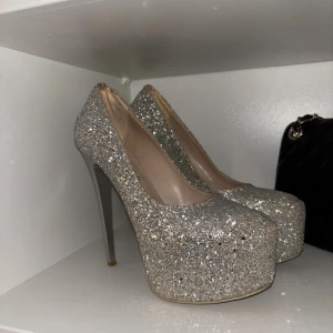 Glittriga silverfärgade pumps med platå - Säljer ett par riktigt snygga pumps i silver med glittrig yta och hög klack. Skorna har rund tå och en rejäl platåsula som ger extra höjd. Använd endast vid ett tillfälle🥰