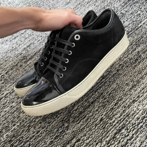 Svarta sneakers från Lanvin med lackad tå - Säljer ett par svarta Lanvin sneakers med snygg kontrast mellan mocka och lackad tå. Skorna har vita platta sulor, svarta snören och rund tå. Klassisk och stilren design som passar till det mesta. Kommer med originalkartong.