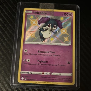 Indedee Pokémonkort - Snyggt Indedee-kort med glittrande effekt! Perfekt för dig som samlar Pokémonkort eller vill boosta din lek med en unik och färgstark karaktär. Kortet är i skyddande plastfodral och har coola attacker som Replenish Time och Psybeam. Ett måste för Pokémonfans!