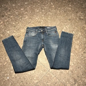 Replay Anbass Slim Fit Jeans Blå - Snygga blå Replay Anbass jeans i slim fit med klassisk femficksdesign och ljus tvätt. Byxorna har raka ben, normal midja och detaljerade bakfickor med Replay-logga på läderpatch. Perfekta för dig som gillar stilrena och bekväma jeans.