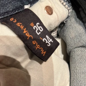 Mörkblå jeans från Nudie Jeans Co W26 L34 - Snygga mörkblå jeans från Nudie jeans co. Jeansen har raka ben och subtila detaljer på bakfickorna. Perfekt passform för dig som gillar stilrena och tidlösa jeans.