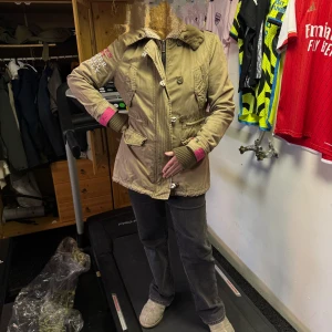  Parkas från Superdry med huva - Säljer en parkas från Superdry med broderad logga på ärmen, mysig teddyfoder i huvan och cool rosa insida och detaljer vid ärmsluten. Jackan har knappar, dragkedja och praktiska fickor. Perfekt för dig som vill ha en snygg och funktionell jacka med streetkänsla.