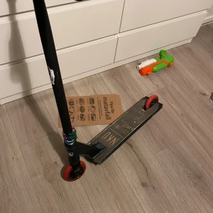 NKD Ride Hard Kick Scooter - NKD Ride Hard kick scooter med robust deck och röda hjul. Synligt slitage på deck och broms, men fullt funktionell. Perfekt för tricks och daglig användning. Passar både nybörjare och erfarna åkare. Säljs i befintligt skick.