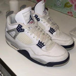 Nike Air Jordan 4 White Cement - Säljer ett par Nike Air Jordan 4 White Cement med klassisk vit ovandel i skinn, grå och svarta detaljer samt specklad mellansula. Ikonisk Jumpman-logga på plösen och hälen. Snygg retrostil med meshpaneler och snörning framtill. Perfekta för dig som gillar streetwear och sneakerskultur.