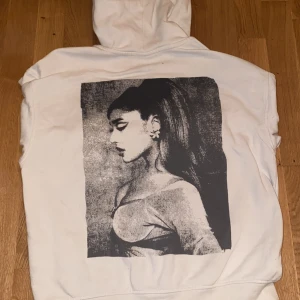 Ariana Grande vit hoodie med tryck - Vit hoodie med dragkedja från Ariana Grande merch, med stort svartvitt tryck av Ariana på ryggen och diskret logga fram. Hoodien har huva, långa ärmar och är gjord i mjuk bomull. Perfekt för dig som älskar ikoniska prints och vill sticka ut. Inte min utan syrrans men kom privat om ni har frågor 🫶🏻🫶🏻passar någon från typ 150-170 kanske 