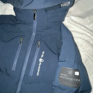 Mörkblå Sail Racing dunjacka &  - En mörkblåa Sail racing jacka storlek 150 säljes. Passar även 160 till 165 skulle jag säga. Använd fåtal gånger.  PRIS EJ HUGGET I STEN! Men har även inte bråttom att sälja.