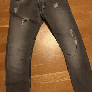 Grå slitna jeans från Pierre Balmain stl 32 - Snygga grå jeans från Pierre Balmain med slitningar och distressed detaljer på både fram- och baksida. Modellen är smal och klassisk femficksdesign. Perfekt för dig som gillar en edgy och modern look.