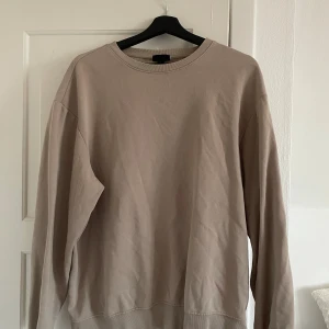Beige sweatshirt med rund hals - En enkel och stilren beige sweatshirt med rund hals och långa ärmar. Tröjan har en loose passform och är tillverkad i mjuk bomull, perfekt för chill dagar. Passar dig som gillar neutrala färger och avslappnad stil.