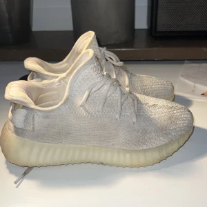 Adidas Yeezy Boost 350 V2 Cream White - Säljer ett par Adidas Yeezy Boost 350 V2 i färgen Cream White. Skorna har en stickad ovandel i syntetmaterial, rund tå och snörning. Den ribbade plattformssulan är i beige ton och ger en unik look. Perfekt för dig som gillar streetwear och vill ha något som sticker ut.