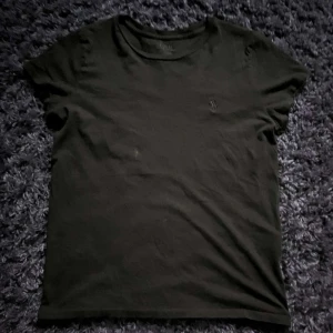 Olivgrön t-shirt från Polo Ralph Lauren - Olivgrön t-shirt från Polo Ralph Lauren med klassisk rund hals och diskret broderad logga på bröstet. T-shirten är i mjuk bomull och har en enkel, stilren design med korta ärmar. Perfekt för en avslappnad look. Har en liten fläck men går att ta bort