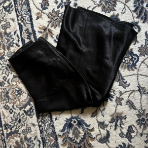 Svart midi satin kjol - Fin svart satin kjol i glansigt satinmaterial. Kjolen har en fin passform på kroppen och känns riktigt lyxiga med sin släta yta. Perfekta för dig som vill sticka ut med en elegant vibe och gillar att mixa material i din outfit. Dessa är helt oanvända pga fel storlek. 