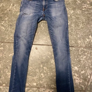 Nudie jeans - Säljer ett par blå nudie jeans för endast 350 kr. Jeansen har en slitning på framsidan. Jeansen är i storlek 30-34. Dessa jeans passar perfekt nu till hösten med sin vintage look.