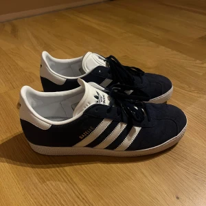 Adidas skor - Modellen heter ”GAZELLE UNISEX - Sneakers - collegiate navy/footwear white”. Använda max 3 gånger, väldigt fint skick men har ett par andra adidas skor därav säljer jag dem. De är i barn storlek, men ändå en storlek 40 som sitter normalt och bekvämt.