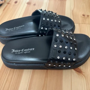 Juicy Couture svarta sandaler med nitar - Svarta sandaler från Juicy Couture med bred rem dekorerad med svarta nitar och glittrande stenar. Snygg chunky sula och logga på fotbädden. Perfekt statement-piece för dig som gillar edgy detaljer