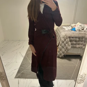 Vinröd kappa från  Twist & Tango - Vinröd kappa Twist & Tango i omlottmodell med knytband i midjan och svarta detaljer. Klänningen har långa ärmar och är tillverkad i ett mjukt ullmaterial. Perfekt för dig som gillar en stilren och trendig look.