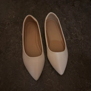 Vita ballerinaskor med spetsig tå - Snygga vita ballerinaskor med spetsig tå och platt sula. Skorna har en stilren design i syntetmaterial och en lätt glansig finish. Perfekta för dig som gillar minimalistisk och trendig stil.