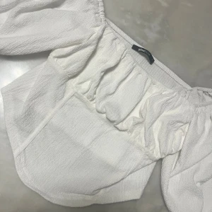 Vit blus med puffärm från Gina Tricot - Säljer en vit blus från Gina Tricot i storlek L. Blusen har puffiga långärmar och en snygg, rynkad detalj vid axlarna. Materialet är strukturerat och känns lätt och luftigt. Perfekt för dig som gillar romantisk och trendig stil.