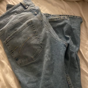 Ljusblå jeans, vida med låg midja från Junkyard, storlek M - Säljer ett par ljusblå jeans från Junkyard i klassisk femficksmodell. Jeansen har raka ben, normal passform och snygga kontrastsömmar. Perfekta för dig som gillar en enkel och stilren look. Materialet är mjukt denim i bomull.