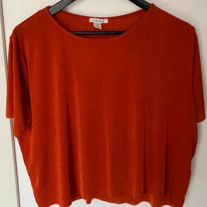 Rostorange ribbad topp från Amisu XS - Säljer en snygg rostorange topp från Amisu i storlek XS. Toppen har en rund halsringning, korta ärmar och ett ribbat tyg som ger en cool struktur. Passformen är loose och materialet känns lätt och skönt mot huden. Perfekt för dig som gillar färg och enkel stil.
