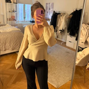 Beige blus  med v-ringning - Säljer en beige blus med v-ringning och långa puffiga ärmar. Blusen har en lätt strukturerad yta och markerad midja som ger en snygg siluett. Perfekt att styla med jeans eller kostymbyxor för en trendig look.