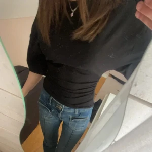 Svart topp från Gina Tricot - Svart topp från Gina Tricot i storlek XS med korta ärmar. Modellen är slim och har snygg rynkning i sidorna som ger en cool och modern siluett. Perfekt till jeans eller kjol för en trendig look.