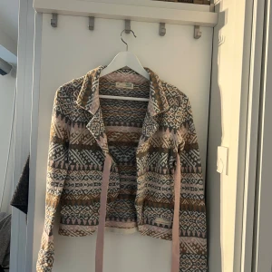 Mönstrad kofta från Odd Molly - Superfin kofta från Odd Molly med snyggt jacquardmönster i grått, beige, rosa och brunt. Koftan är stickad, har långa ärmar, krage och knytband framtill. Perfekt för lager-på-lager och ger en cool boho-vibe till din outfit.