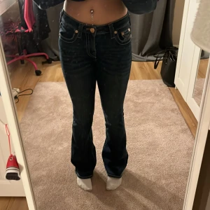 True Religion jeans med rosa detaljer - Mörkblå True Religion jeans i modellen Becca. Jeansen är mid waist och väldigt sköna med stretchigt material. Perfekta nu till hösten! Rosa detaljer på bakfickorna. Bra skick men lite slitna ner till på vänster byxben.
