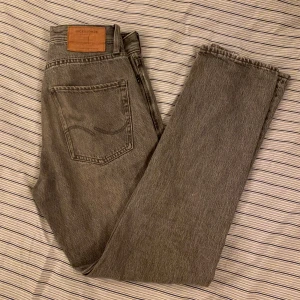 Gråa jeans från Jack & Jones - Säljer ett par gråa jeans från Jack & Jones, modell Relaxed/Chris. Jeansen har klassisk femficksdesign, raka ben och normal passform. Materialet är denim i bomull och de har råa, avklippta benslut för en avslappnad look. 28/32
