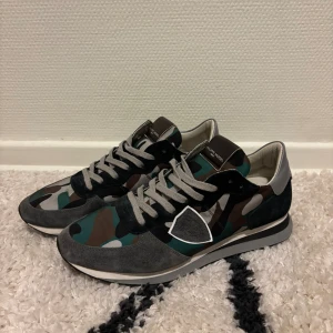 Camo Philippe Model Trpx trainers - Säljer dessa riktigt feta Philippe Model trainers i storlek 42. Dem har riktigt snygg sällsynt camo detalj som matchar bra med den gråa loggan samt resten av skon. Passar perfekt nu mot hösten och lite ruskigare väder. Säljer då jag inte aldrig använt skon så mycket och därav det fina skicket, skulle gissa på ca 15 användningar och sulan är i så gott som nyskick. Låda och kort medföljer. Tveka inte vid frågor eller prisförslag🦤🍁👞.