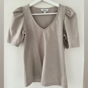 Glittrig topp från Kappahl - Champagnefärgad glittrig topp från Kappahl med v-ringning och puffade korta ärmar. Toppen är så fin och i nästintill nyskick! 