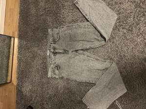 Grå tvättade jeans från Woodbird - Säljer ett par grå tvättade jeans från Woodbird med klassisk femficksdesign och dragkedja. Jeansen har en rak passform med något smalare ben och normal midja. Materialet är robust denim i bomull och färgen är snyggt stentvättad grå.