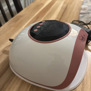 Sofi Nails 4S UV LED Nagellampa - Sofi Nails 4S UV LED nagellampa i vitt och rosa, perfekt för gel- och shellacmanikyr. Flera timerinställningar och medföljande strömadapter. Lampan är i gott skick med mindre ytliga repor, fungerar utmärkt för professionell eller hemmabruk.