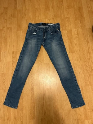 Blå Replay jeans slim fit - Säljer ett par snygga blå jeans från Replay i modellen slim fit. Jeansen har klassisk femficksdesign, ljusa slitningar och raka ben. Materialet är stretchigt denim med inslag av elastan för extra komfort. Perfekt för dig som gillar stilrena och moderna jeans.