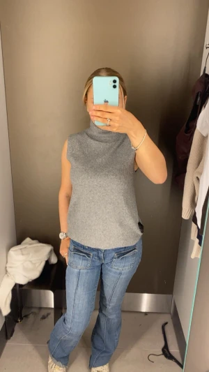 Grå ärmlös polotröja - Säljer en stilren grå ärmlös polotröja i mjukt stickat material. Perfekt att matcha med jeans eller kjol för en clean look. Hög krage och rak passform ger en modern vibe.