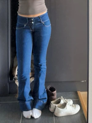 Lågmidjade blå jeans  - Säljer dessa Lågmidjade blåa jeansen, de har två knappar upp till och lite detaljer vid benen. Använt dom fåtal gånger! 