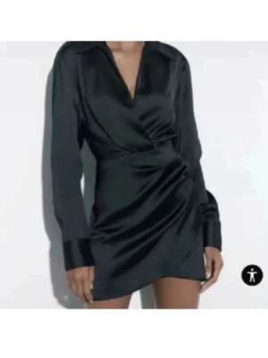  Ny Svart omlottklänning i satin från Zara - Supersnygg svart kort omlottklänning från Zara i glansigt satinmaterial. Klänningen har lång ärm, v-ringning och markerad krage. Snygga detaljer med drapering i midjan och breda manschetter. Perfekt för dig som vill ha en stilren och trendig look.