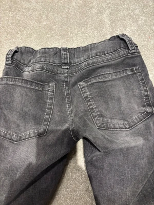 gråa jeans från Gina Tricot, stl 152 - Snygga svarta jeans från Gina Tricot i storlek 152. Jeansen har klassisk femficksdesign, bälteshällor och utsvängda ben. Materialet är mjukt denim med en lätt tvättad look och kontrastsömmar. Perfekta för en avslappnad och cool stil.