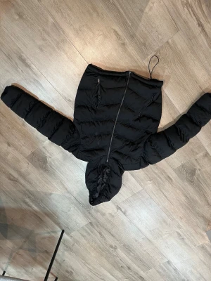 Svart pufferjacka från Fr Sister  - Svart pufferjacka från Fr Sister Basic i storlek XL. Jackan har huva, två framfickor med dragkedja och quiltad design. Perfekt för kalla dagar med sin fluffiga look och långa ärmar. Stängs med dragkedja framtill och har en loose passform. Sitter som en Medium ungefär på tjej.